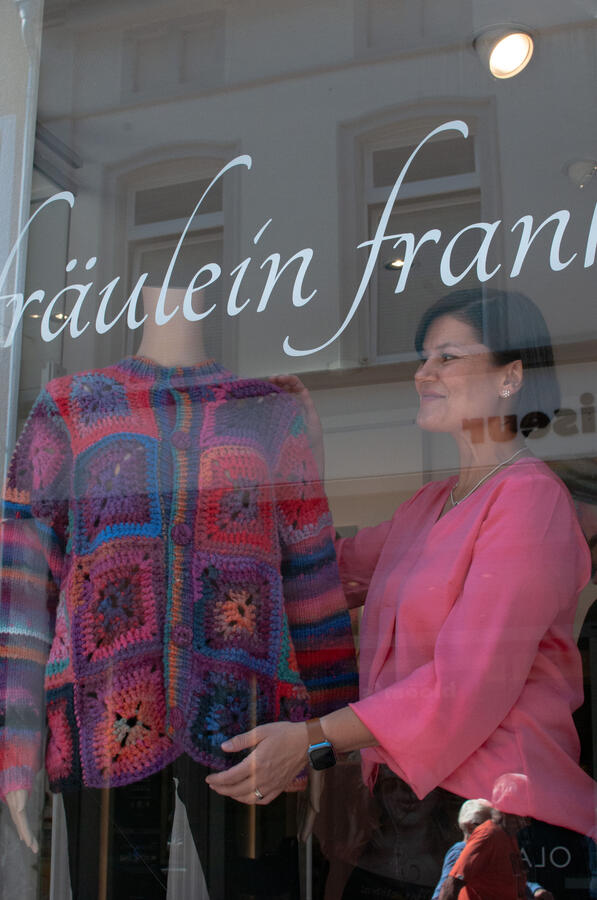 Inhaberin steht im Schaufenster und dekoriert die neue Winterkollektion.