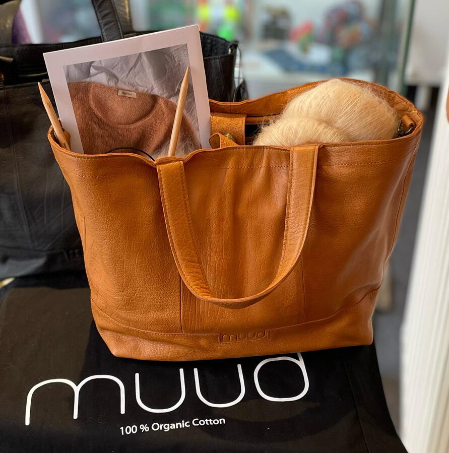 Große und geräumige Handarbeitstasche aus hellbraunem Leder steht im Vordergrund.