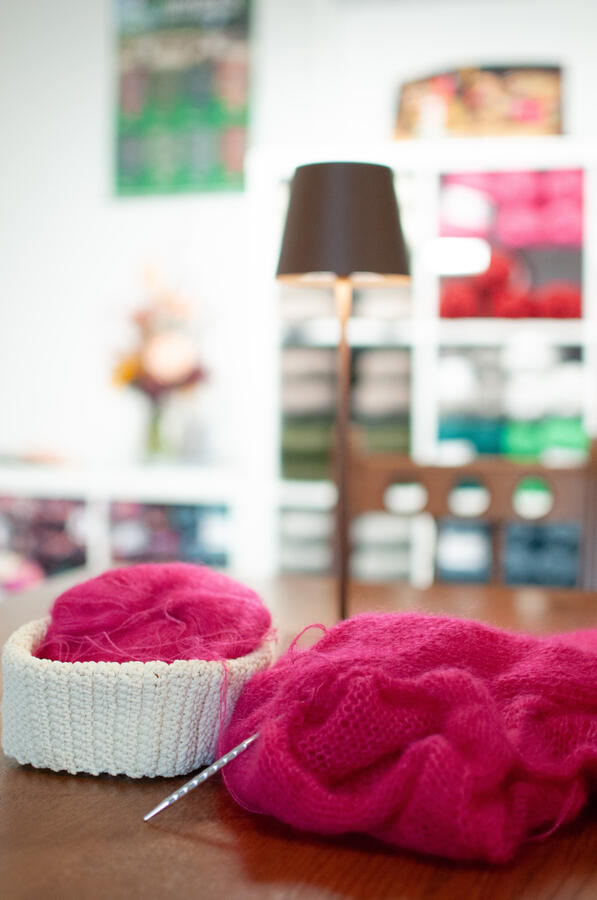 Im Vordergrund sieht man pinke Wolle auf dem Handarbeitstisch.