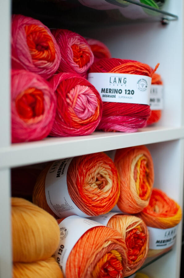 Ausschnitt aus dem Wollregal, man sieht rot-, rosa- und gelbfarbige Wollknäuel.