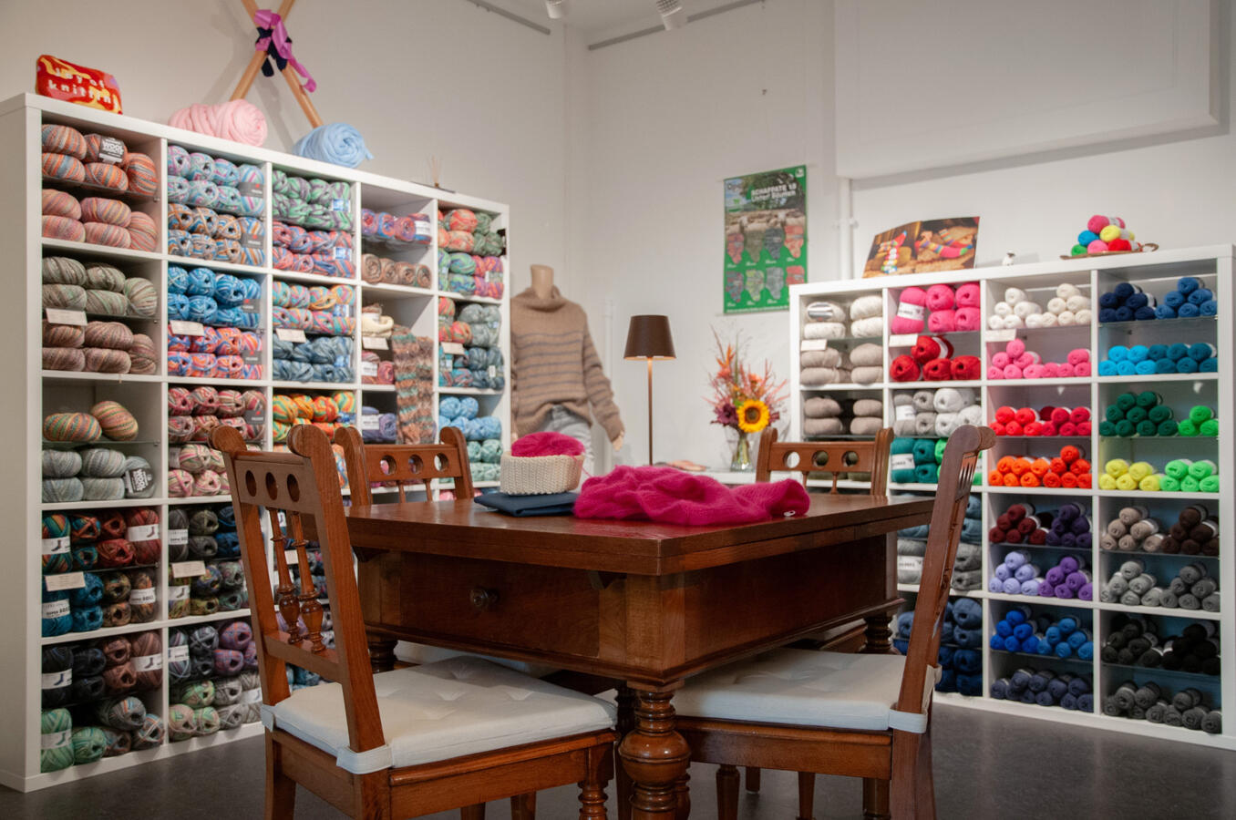 Der große Handarbeitstisch ist im Vordergrund zu sehen, im Hintergrund erkennt man die bunten Wollknäuel ordentlich im Regal.