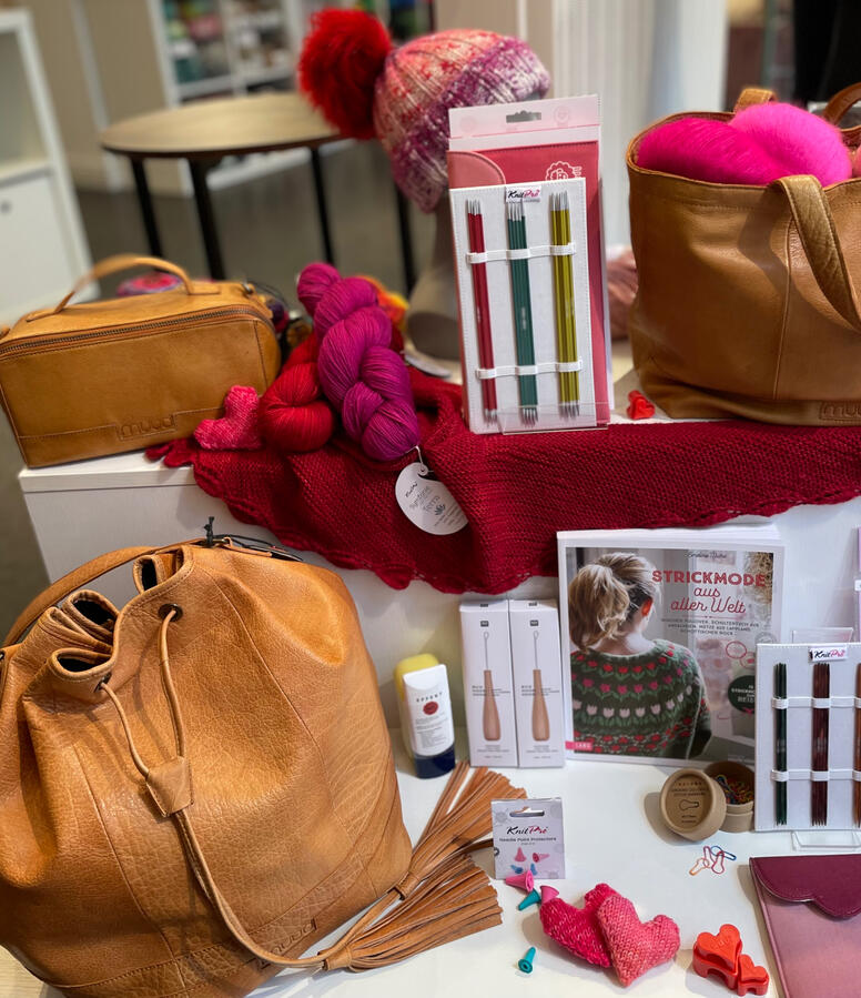 Zu sehen sind verschieden Handarbeitstaschen aus Leder und eine kleine Auswahl an handgefärbten Sockengarnen in Pink- und Rottönen.