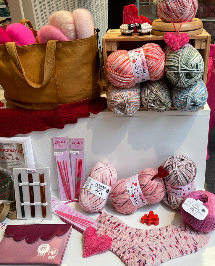 Zu sehen sind verschieden Sockengarne in pink und rosa. Sowie Stricknadeln und eine Handarbeitstasche.