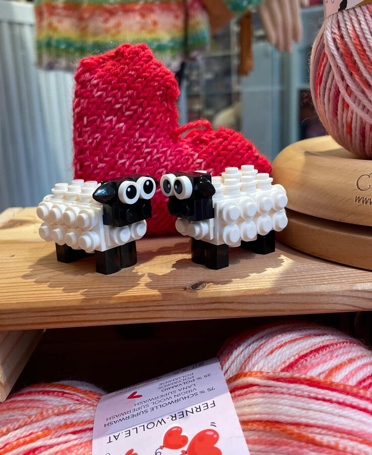 Zu sehen ist ein Schäfchenpaar aus Klemmbausteinen, der Hintergrund ist dekoriert mit einem gestrickten Herz.